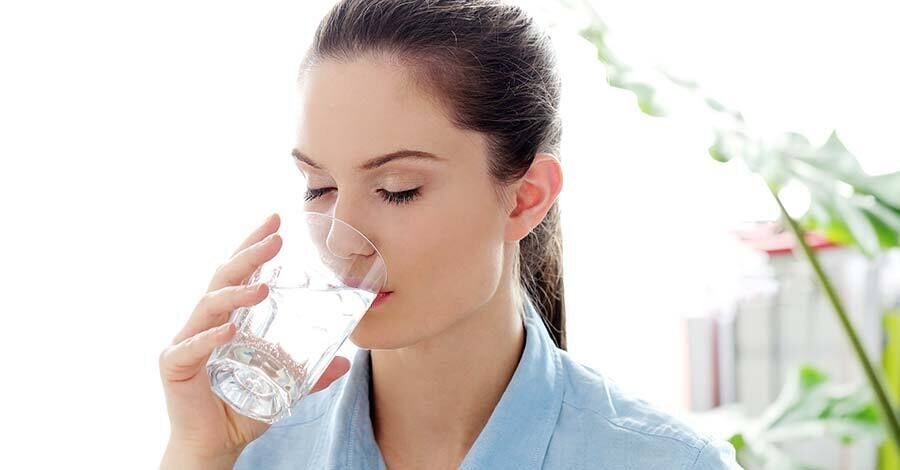 Mujer de ojos cerrados bebiendo agua de un vaso