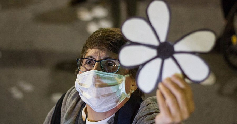 Señora de tapabocas levantando una margarita a la cual le falta un pétalo y representa a los desaparecidos en época de dictadura